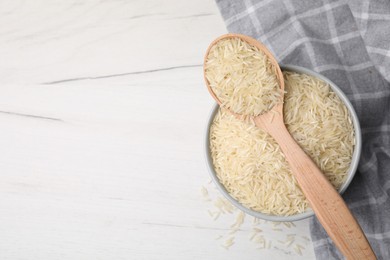 Bowl and spoon with raw rice on white wooden table, top view. Space for text