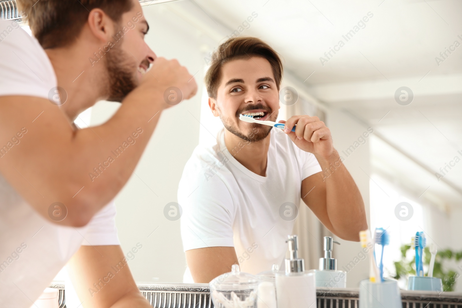 Photo of Young man with toothbrush near mirror in bathroom. Personal hygiene