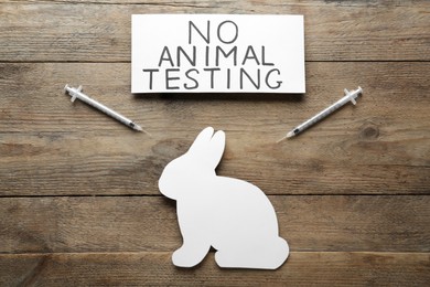 Card with text No Animal Testing, figure of rabbit and syringes on wooden table, flat lay