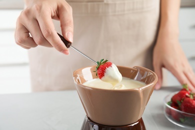 Photo of Woman dipping ripe strawberry into bowl with white chocolate fondue on table