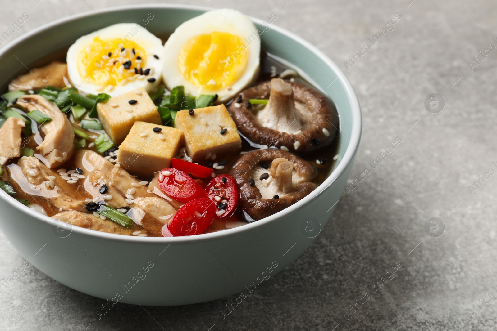 Photo of Bowl of delicious ramen on grey table. Noodle soup