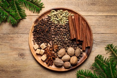 Different spices, nuts and fir branches on wooden table, flat lay