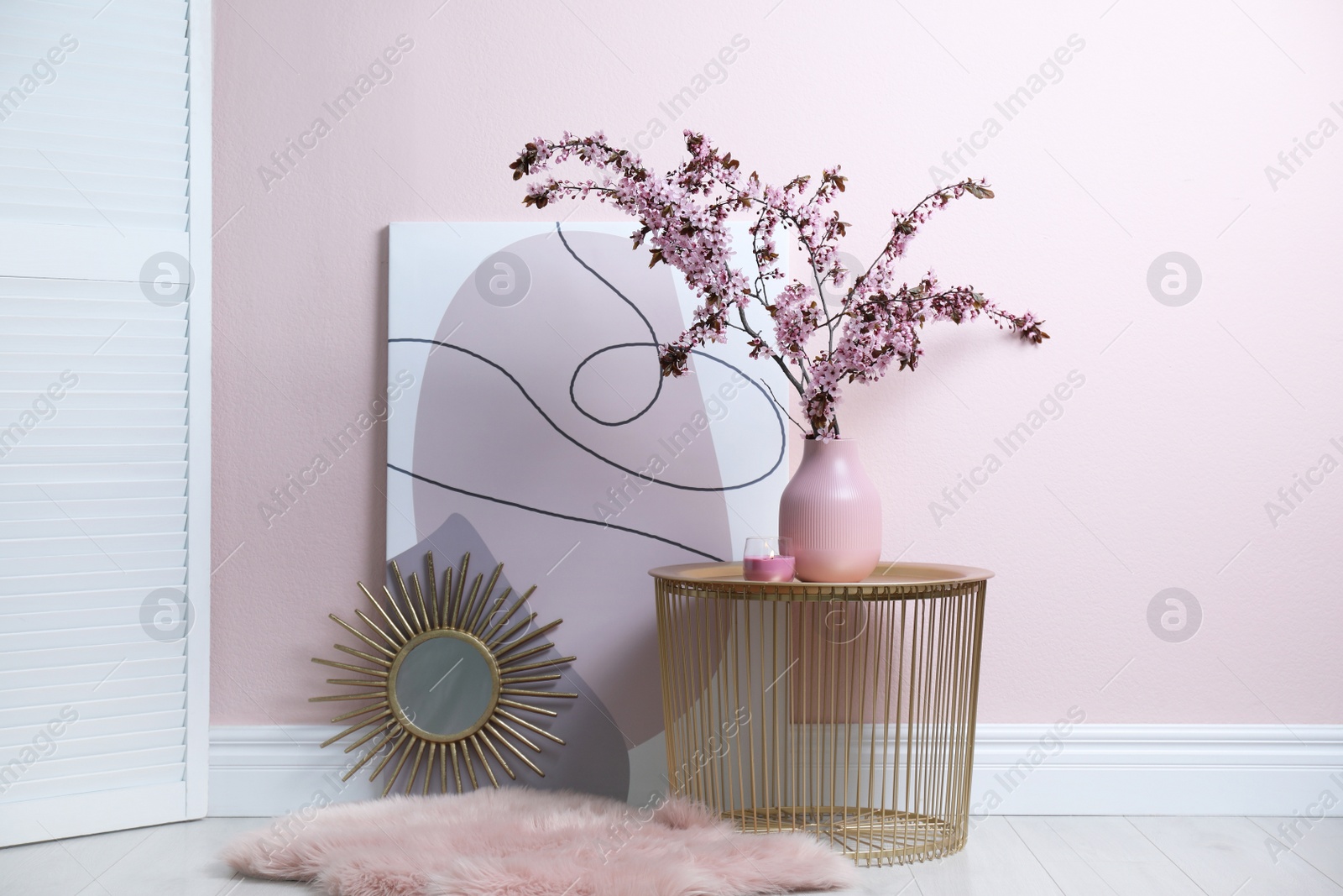 Photo of Blossoming tree twigs in vase on table near pink wall indoors