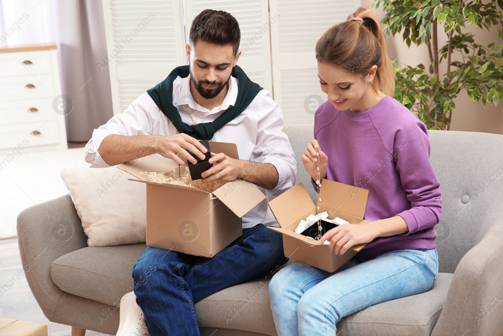 Photo of Young couple opening parcels on sofa in living room