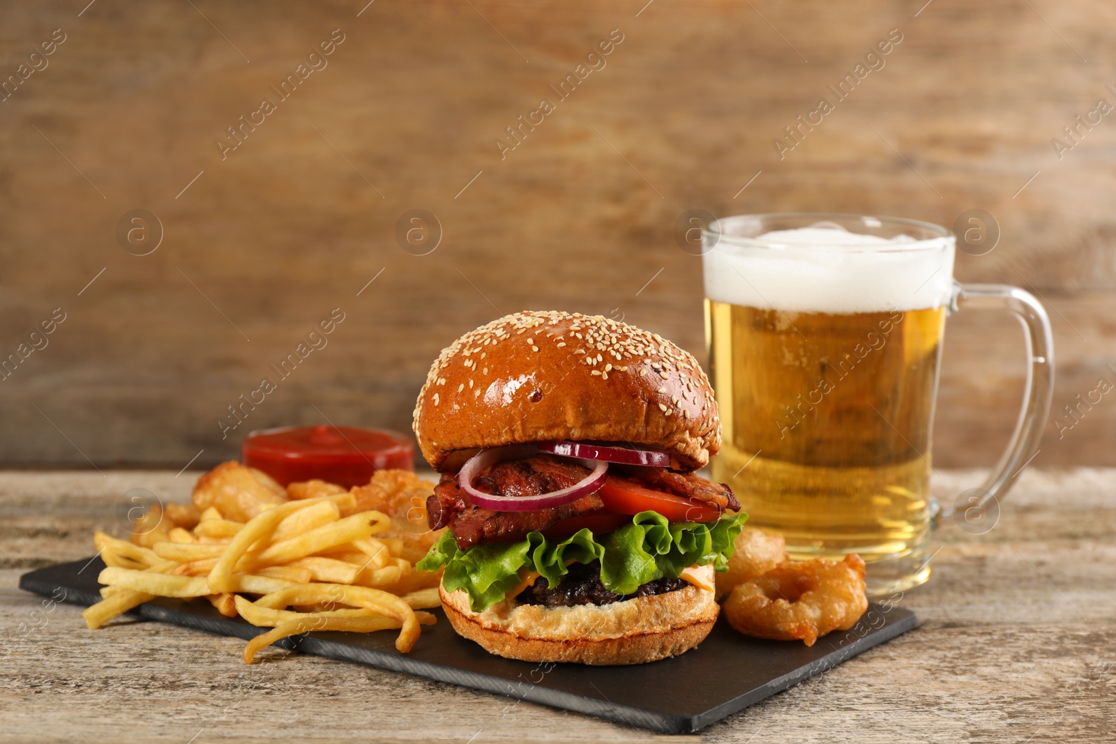 Photo of Tasty burger, French fries, fried onion rings and beer on wooden table. Fast food