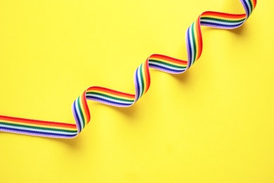 Photo of Rainbow ribbon on yellow background, top view. Gay symbol