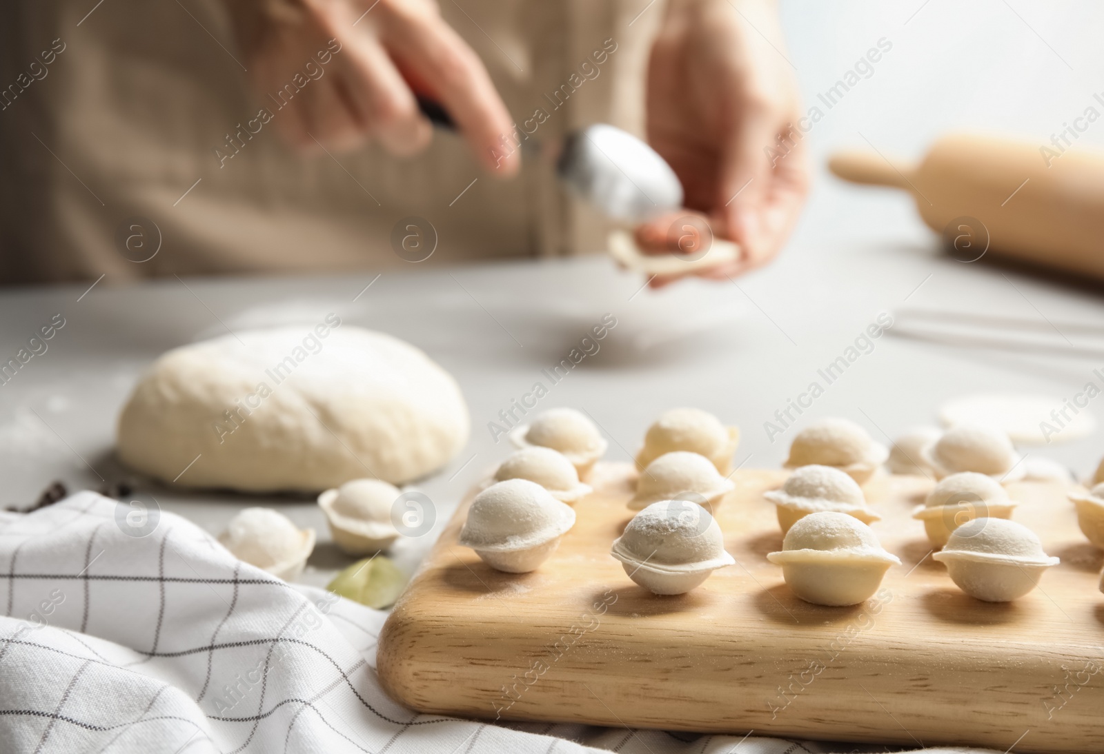 Photo of Wooden board with raw dumplings and blurred woman on background, closeup