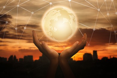 Image of Global innovation. Woman holding virtual planet against cityscape at sunrise, closeup