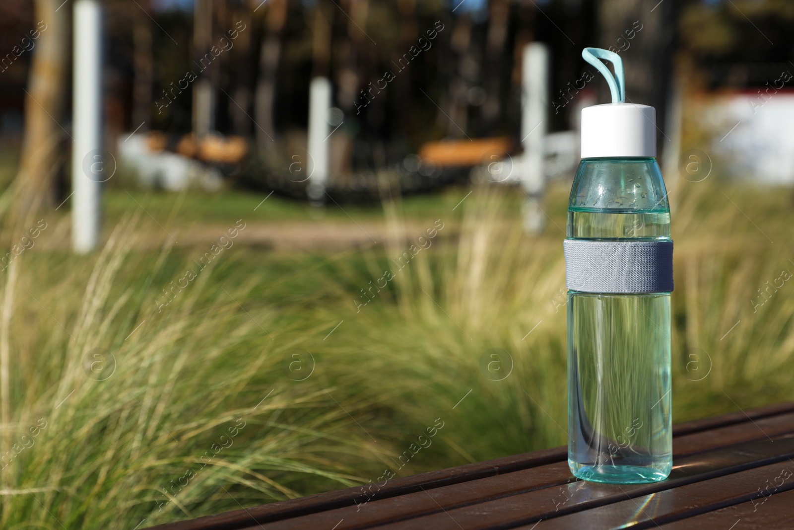 Photo of Glass bottle with water on wooden surface outdoors. Space for text