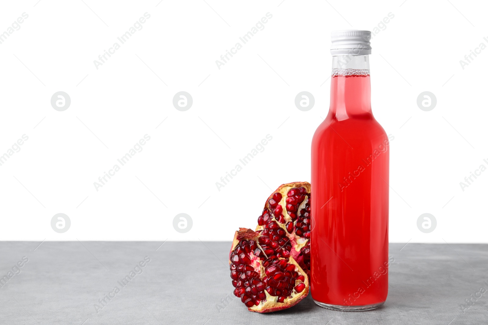 Photo of Delicious kombucha in glass bottle and pomegranate on grey table against white background, space for text