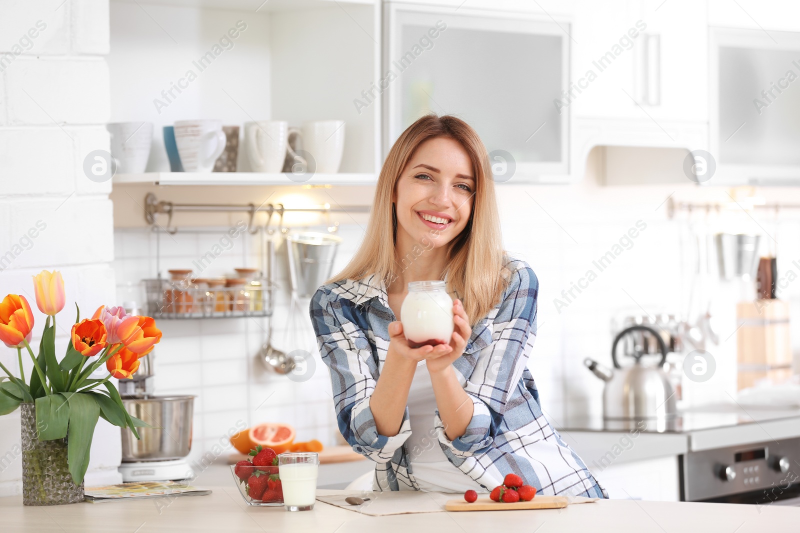 Photo of Young woman with tasty yogurt at table in kitchen