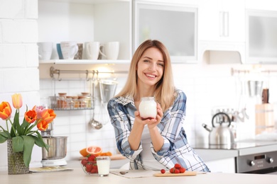 Photo of Young woman with tasty yogurt at table in kitchen