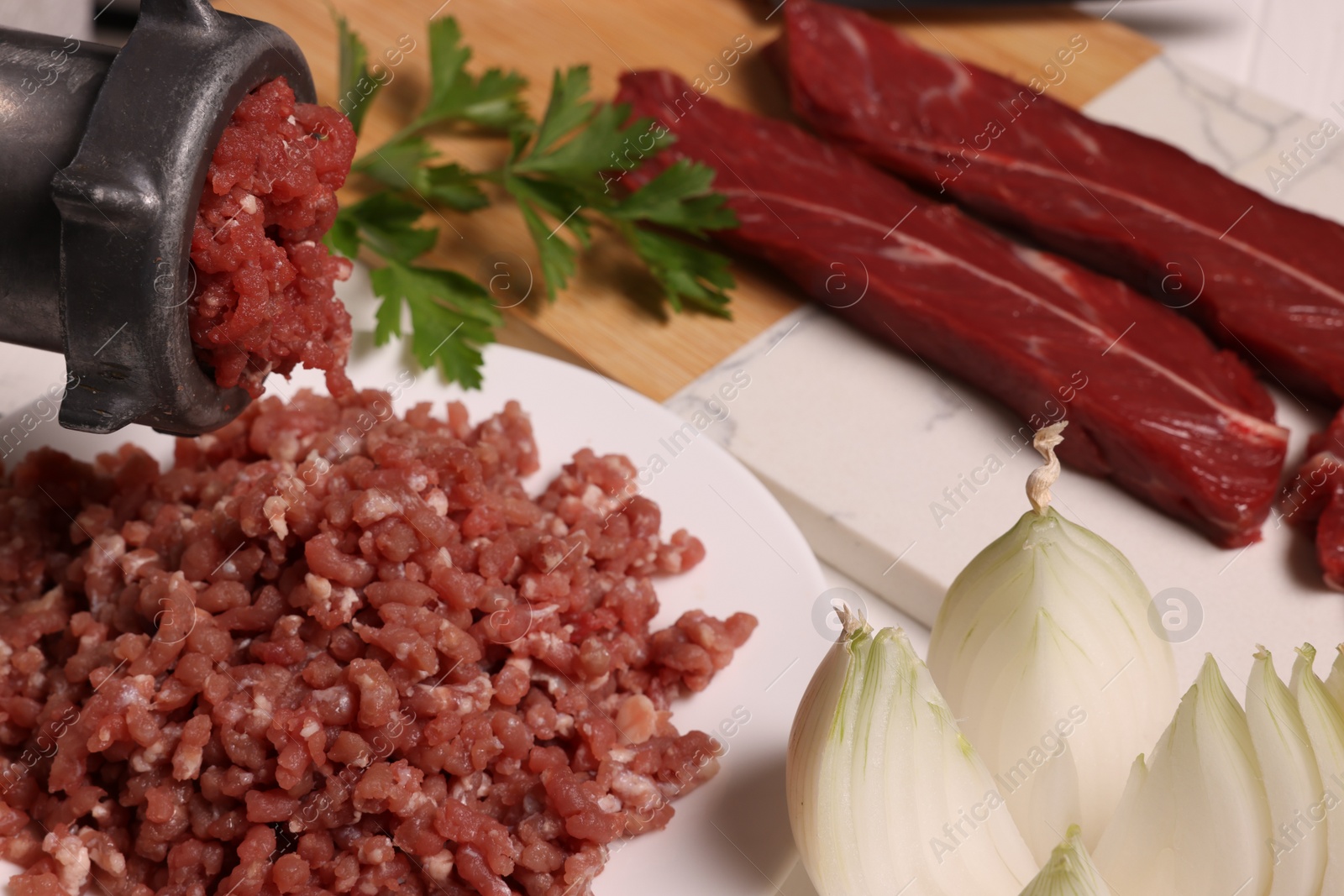 Photo of Manual meat grinder with beef and onion on white table, closeup. Space for text