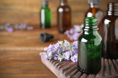 Bottles of essential oil and lavender flowers on wooden table. Space for text