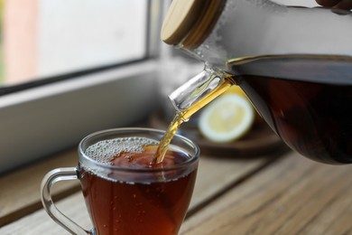 Pouring delicious tea into glass cup on table, closeup