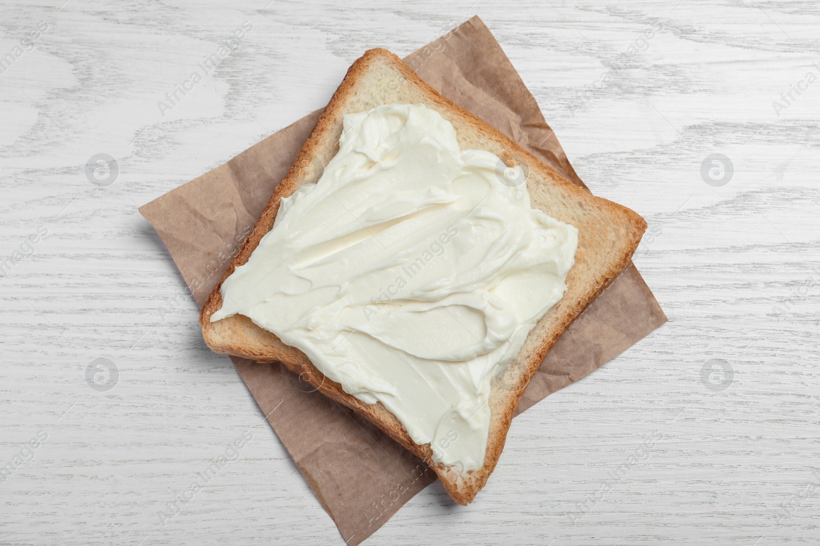 Photo of Slice of bread with tasty cream cheese on white wooden table, top view