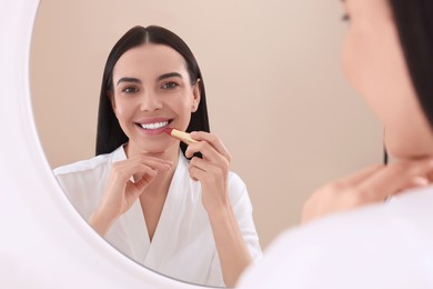 Photo of Beautiful young woman applying lipstick near mirror indoors