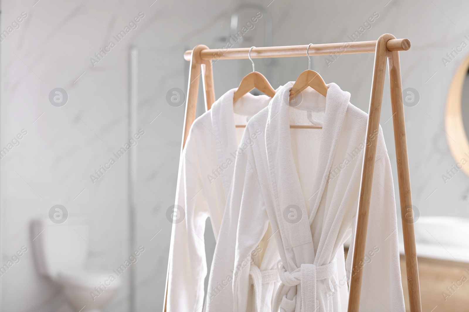Photo of Fresh white bathrobes hanging on rack indoors