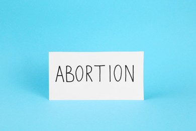 Photo of Paper note with word Abortion on light blue background