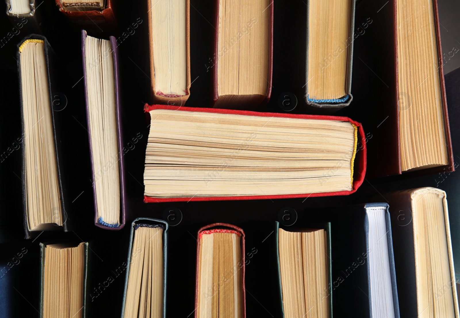 Photo of Many different hardcover books on dark background, top view