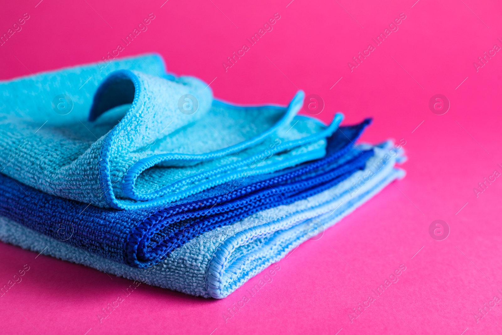 Photo of Stack of blue microfiber cloths on pink background, closeup