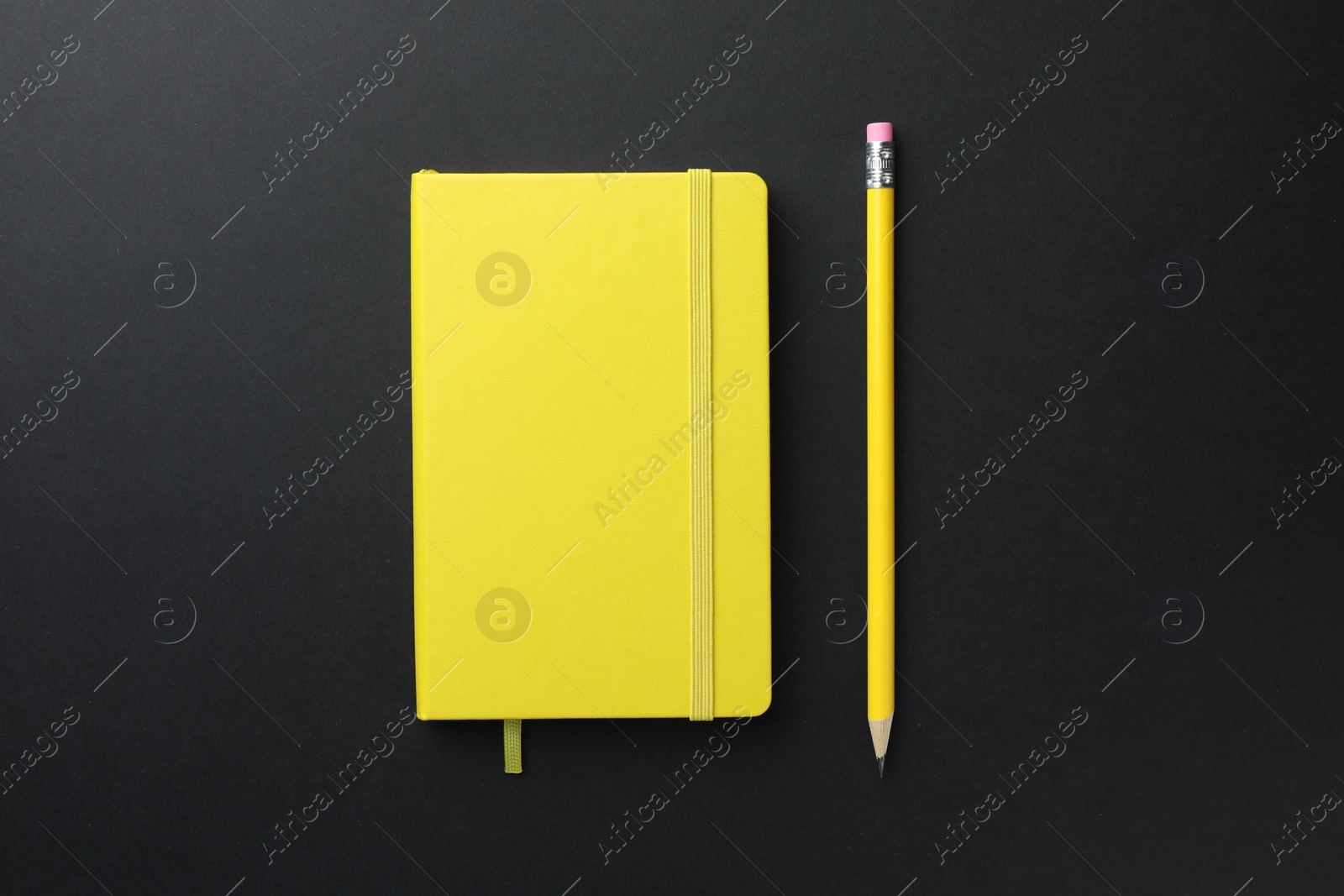 Photo of Closed yellow notebook and pencil on black background, top view