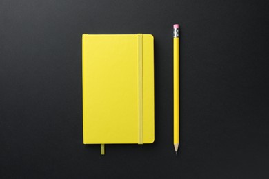 Photo of Closed yellow notebook and pencil on black background, top view