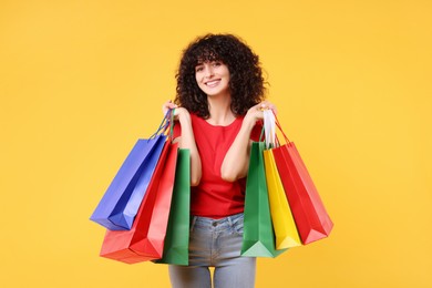 Happy young woman with shopping bags on yellow background