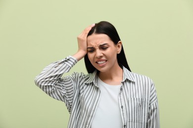 Photo of Woman suffering from migraine on light green background