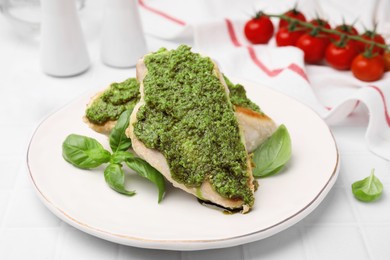 Photo of Delicious chicken breasts with pesto sauce and basil on white tiled table