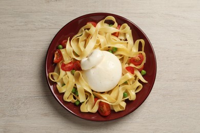 Plate of delicious pasta with burrata, peas and tomatoes on white wooden table, top view