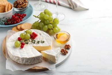 Photo of Brie cheese served with honey and berries on white marble table. Space for text