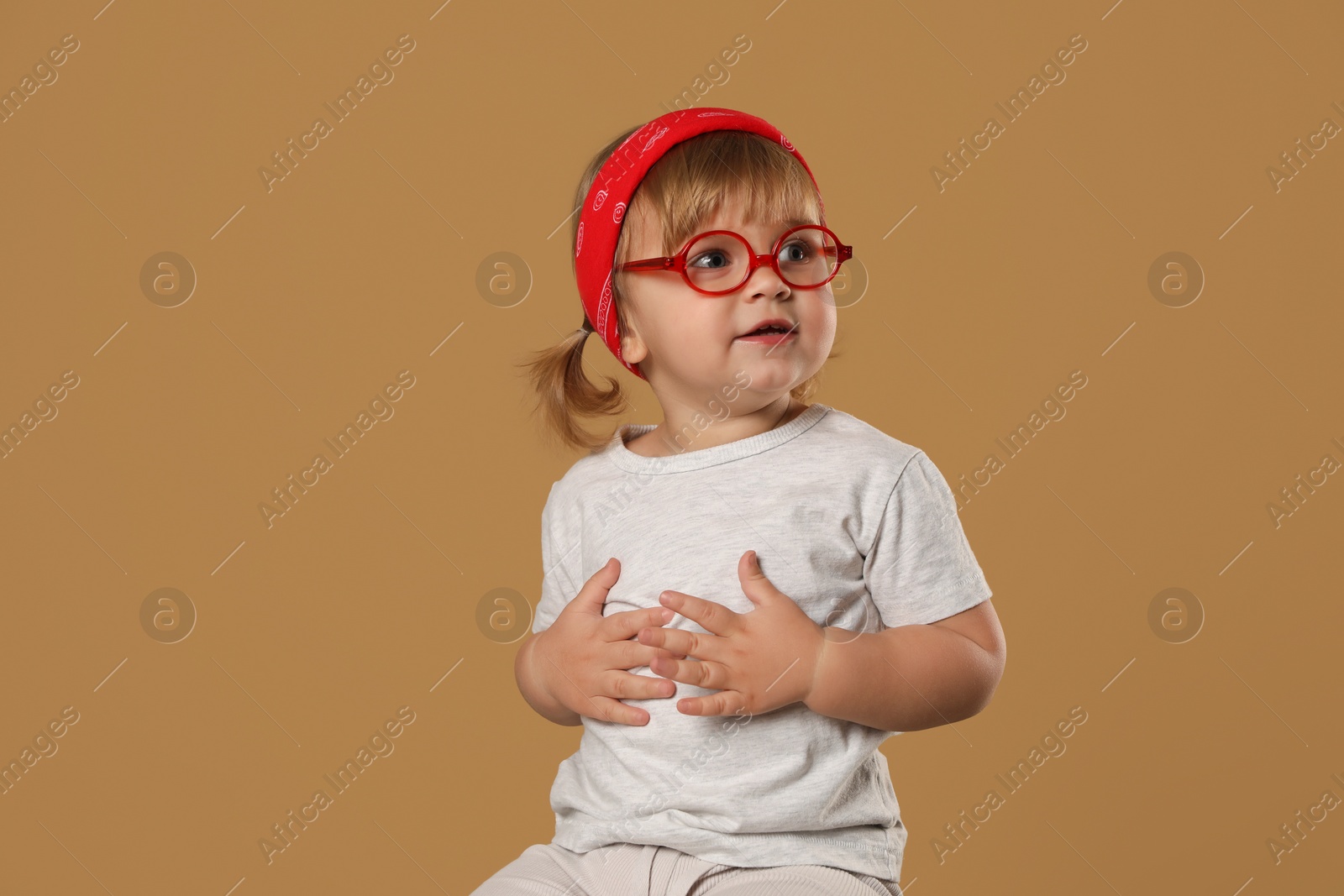 Photo of Cute little girl in glasses on pale brown background