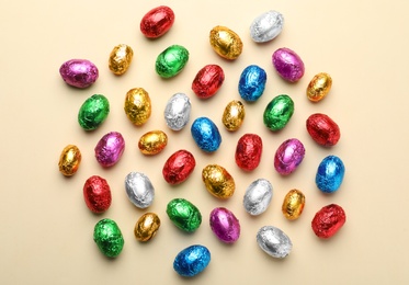 Chocolate eggs wrapped in colorful foil on beige background, flat lay