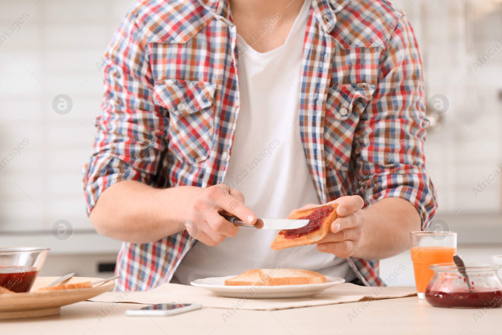 Photo of Young man spreading jam on tasty toasted bread at table in kitchen