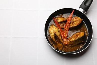 Photo of Tasty fish curry in frying pan on white tiled table, above view. Space for text. Indian cuisine