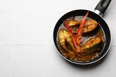 Tasty fish curry in frying pan on white tiled table, above view. Space for text. Indian cuisine