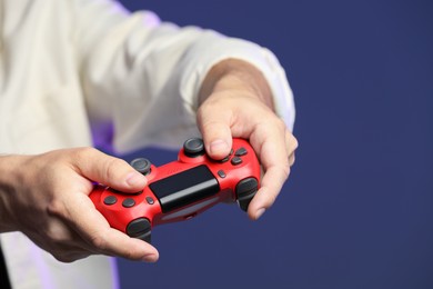 Man playing video game with controller on dark blue background, closeup. Space for text