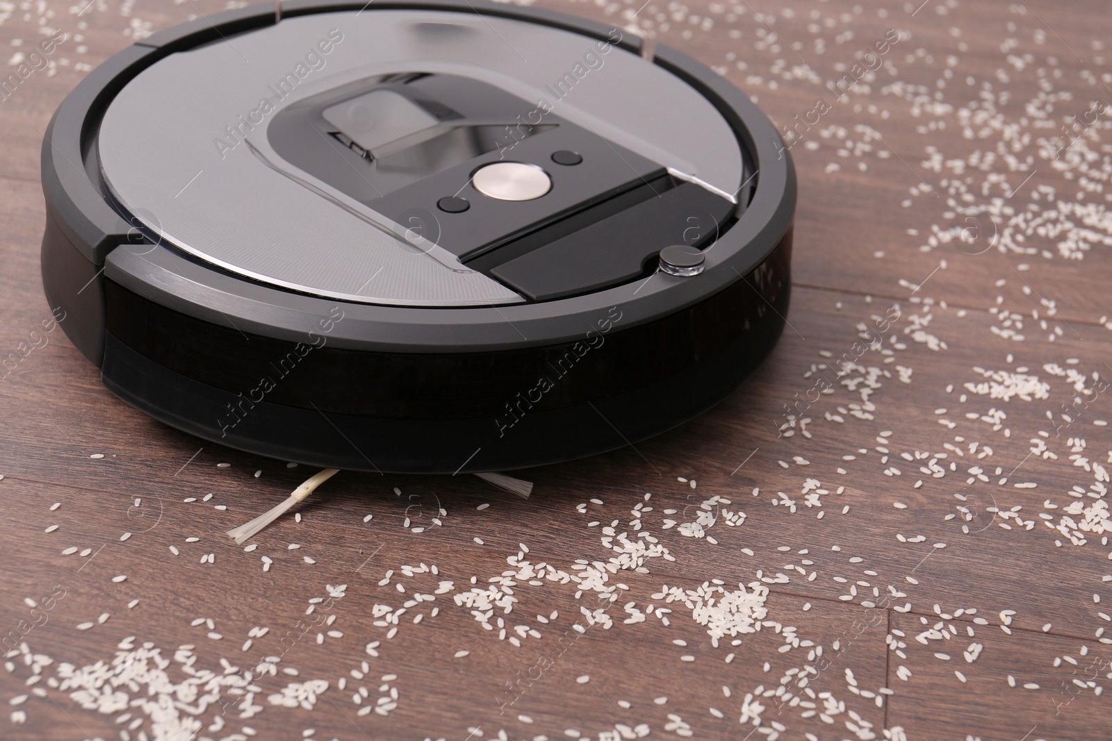 Photo of Removing groats from wooden floor with robotic vacuum cleaner at home, closeup