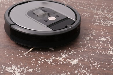 Photo of Removing groats from wooden floor with robotic vacuum cleaner at home, closeup