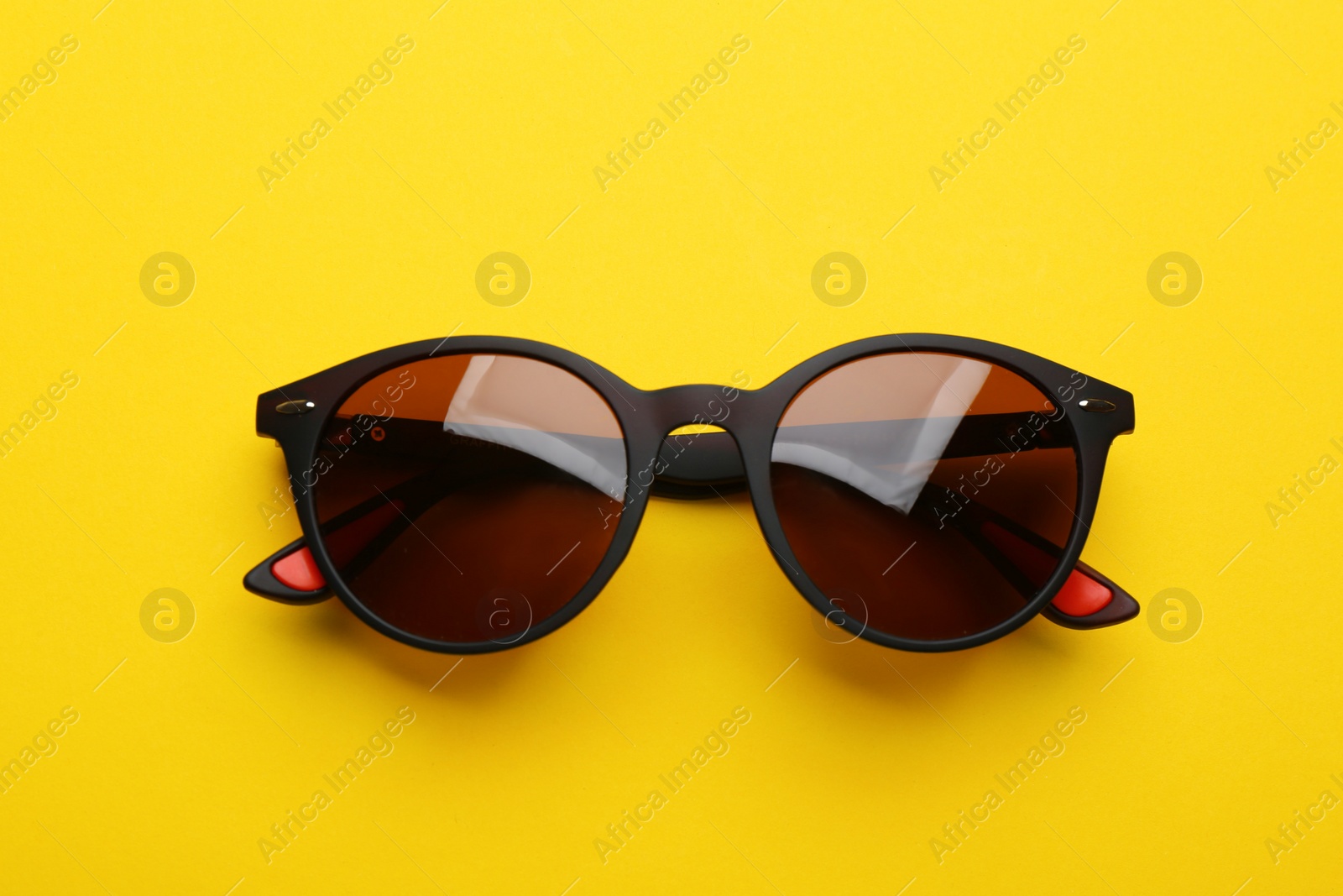 Photo of Stylish sunglasses on yellow background, top view. Fashionable accessory