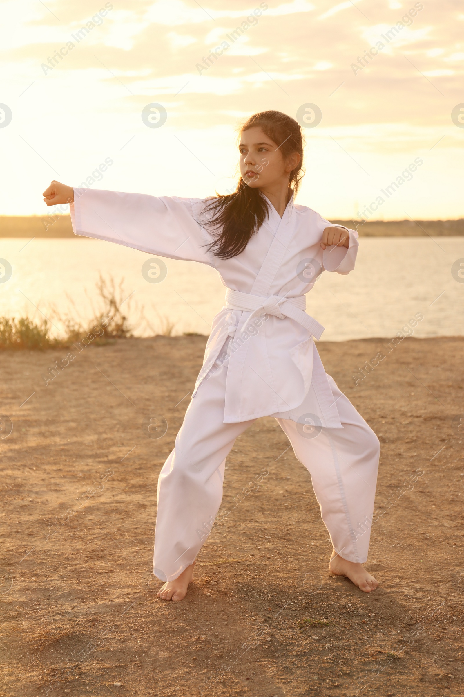 Photo of Cute little girl in kimono practicing karate near river at sunset