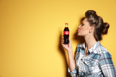 Photo of MYKOLAIV, UKRAINE - NOVEMBER 28, 2018: Young woman with bottle of Coca-Cola on color background, space for text