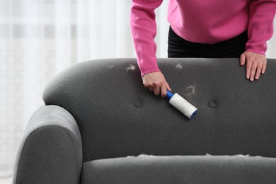 Photo of Woman with lint roller removing pet hair from sofa at home, closeup