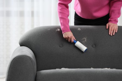 Woman with lint roller removing pet hair from sofa at home, closeup