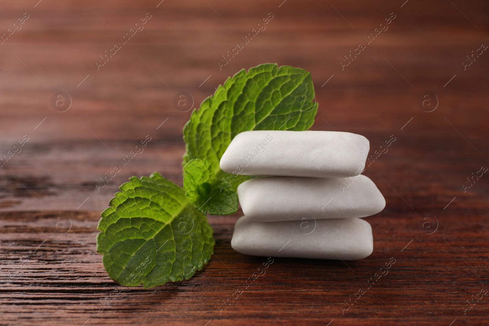 Photo of Tasty white chewing gums and mint leaves on wooden table, closeup