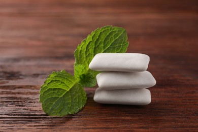 Tasty white chewing gums and mint leaves on wooden table, closeup