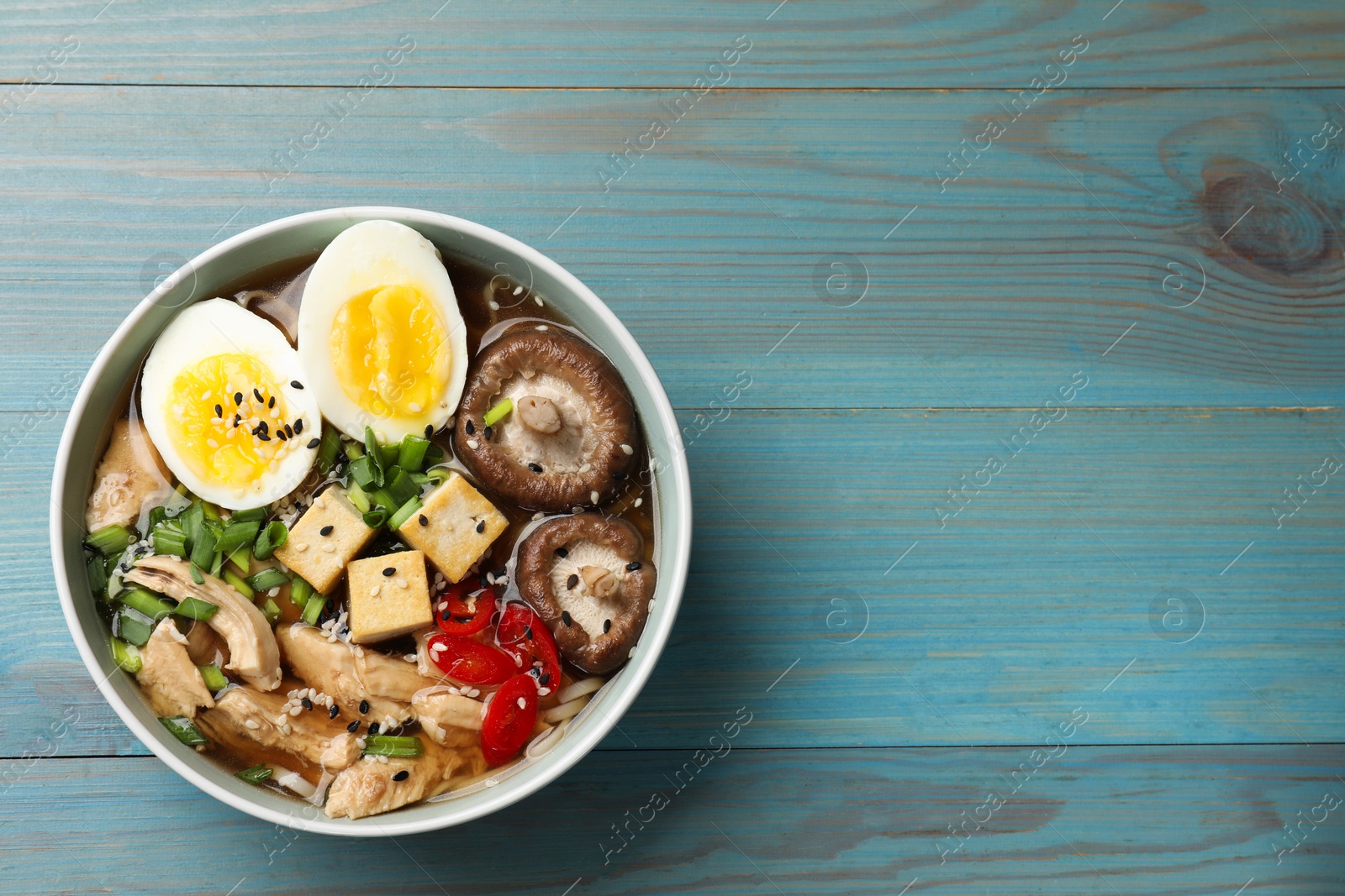 Photo of Bowl of delicious ramen on light blue wooden table, top view with space for text. Noodle soup