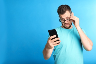 Photo of Man with vision problems using smartphone on blue background, space for text