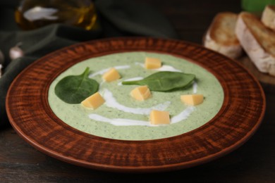 Delicious spinach cream soup with leaves and cheese in bowl on wooden table, closeup